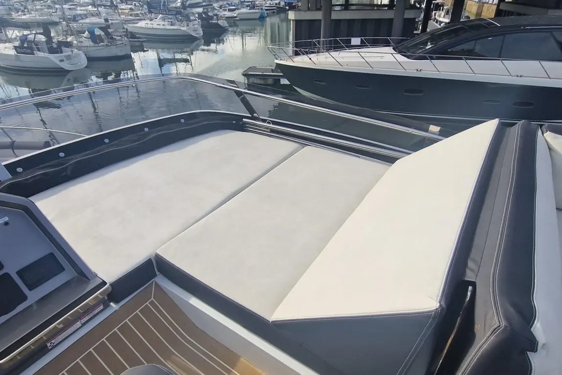 A luxury boat deck featuring a cushioned seating area and a view of parked boats in a marina under clear skies.